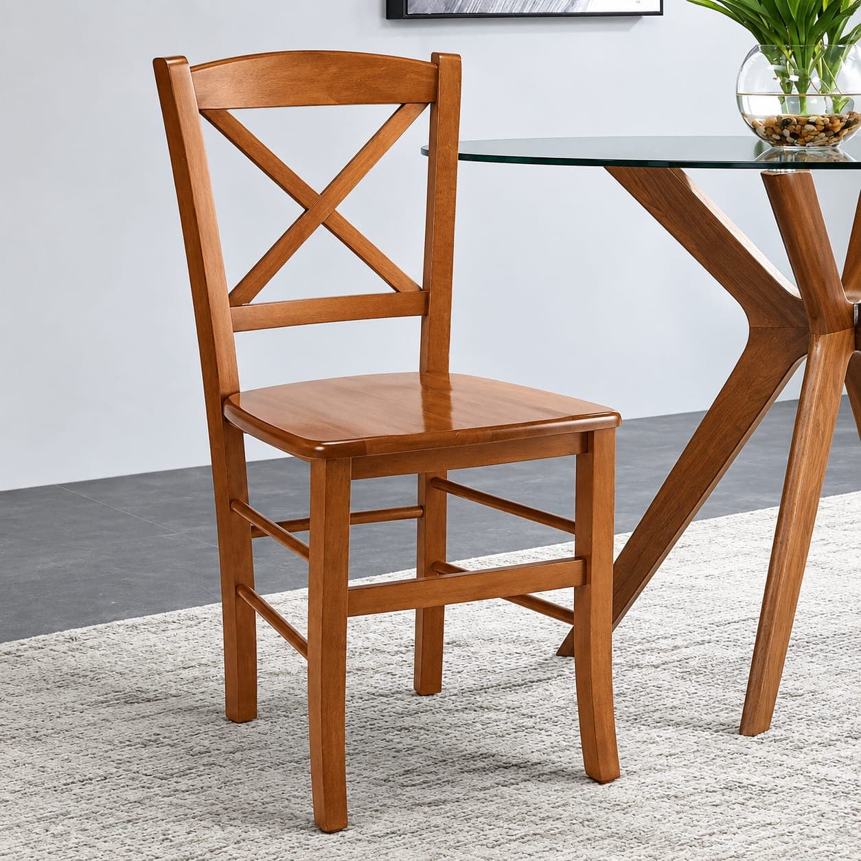 Venezia X cross-back dining chair in warm-toned solid wood with a shaped wooden seat, beside a glass dining table