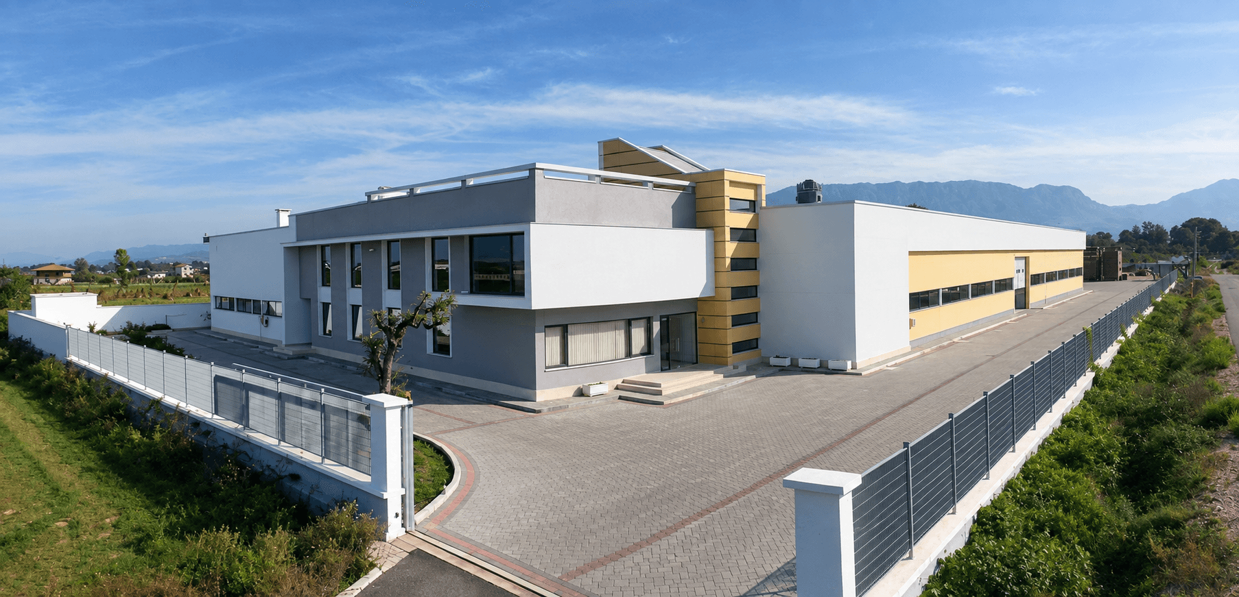 Edi Sedia modern factory building with a gated paved yard and mountains in the background